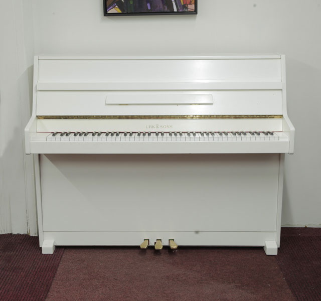 Urk & Sons  VU 110   upright piano with a white gloss case. Piano has an eighty-eight note keyboard and three pedals.
